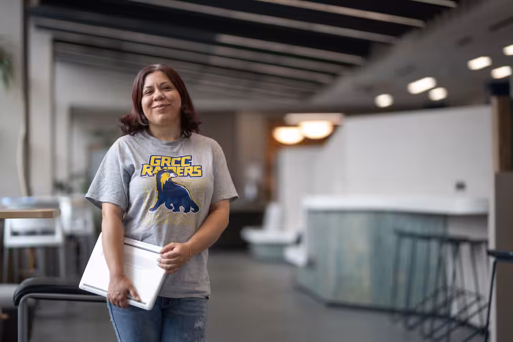 GRCC student wearing a Raiders shirt holds a laptop.