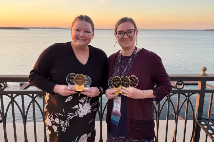 Two members of the marketing team pose holding seven awards.