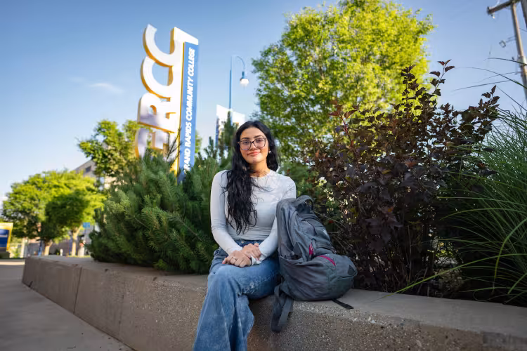 Student sits outside in front of a GRCC campus sign.