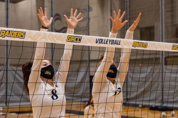 Volleyball players leaping to block a shot.