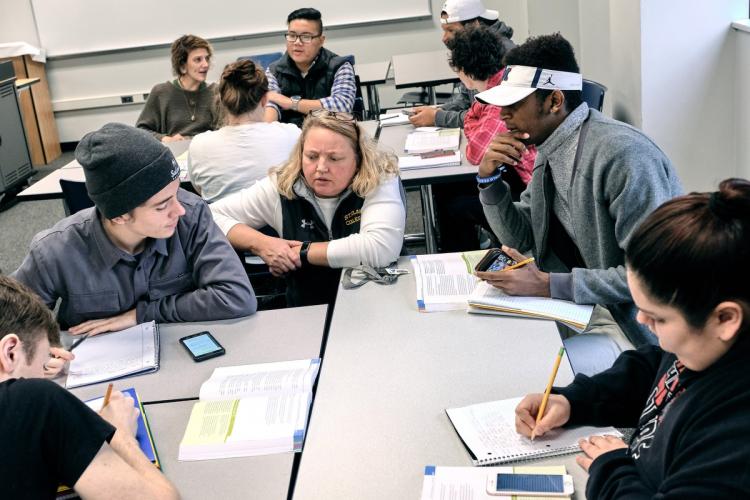 Adjunct English instructor Kaari Bloedow sits with students around a classroom table.