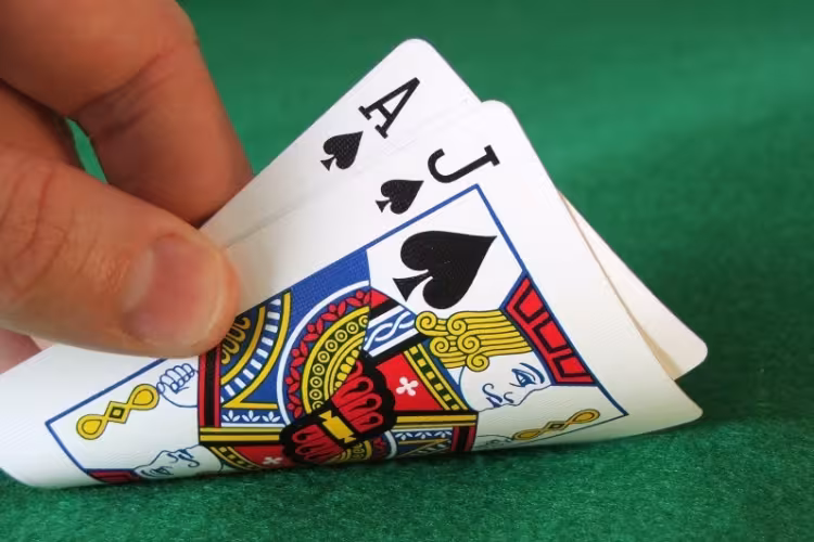 A hand is turning over two cards: the ace and jack of Spades.