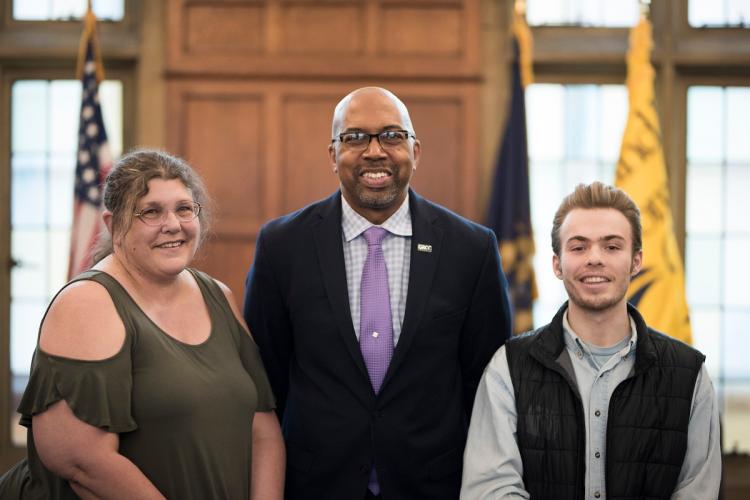 Kelly Burrows and Elijah Paparella stand with President Bill Pink in the board of trustees meeting room.
