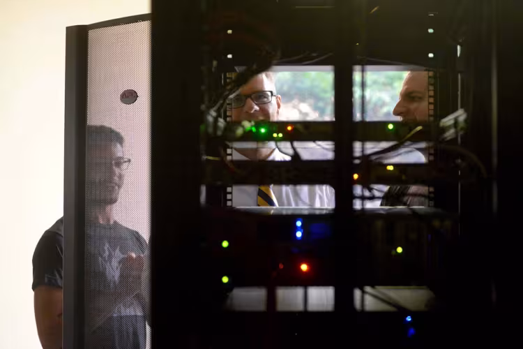 GRCC students and professor looking at a computer server, viewed from the back.