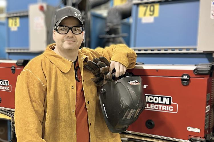 Cory Stout posing with his welding gear in the lab. 