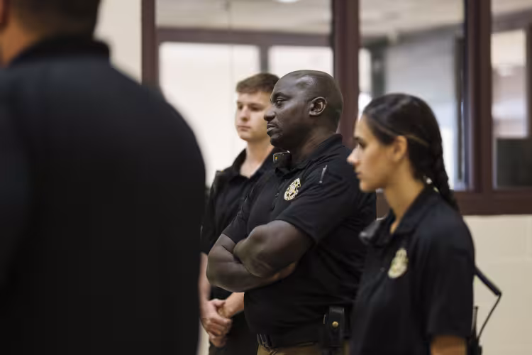 Three people in uniforms and badges stand facing the same direction. 