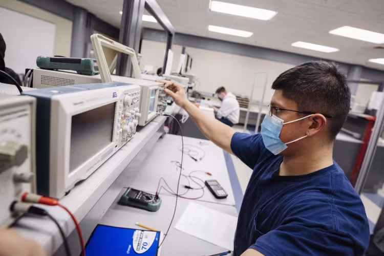 Student wearing a face covering working in an electronics lab.