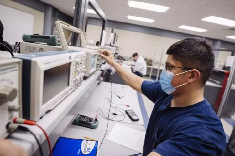 Student wearing a face covering working in an electronics lab.