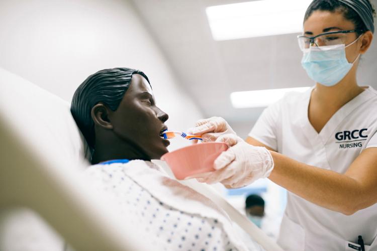 A nursing student brushes the teeth of a plastic model patient. 