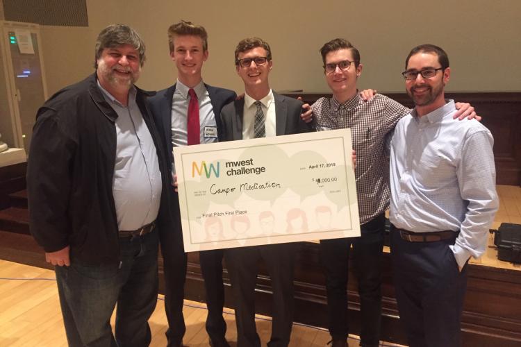 GRCC professor Felix Pereiro stands with ), Aiden Wysocki, Jake Dabkowski, Matthew Veenhoven and Jonathan Moroney, who all hold a giant check.