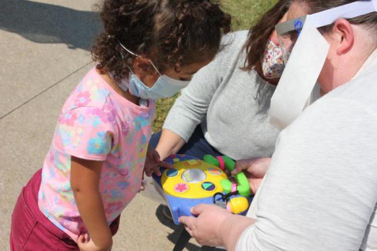 A preschool students looks at her new adaptive toy with a GRCC professor and teacher looking on.