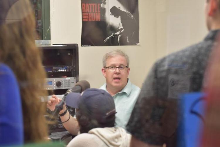 Len O'Kelly sitting in a broadcast booth surrounded by students.