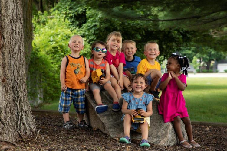 Children sit on a rock in a park.