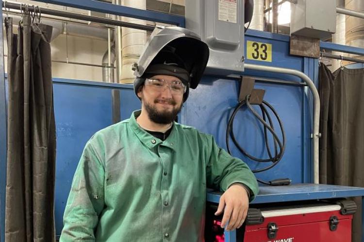 Sam Thomet in the welding shop wearing his protective helmet and shop coat.