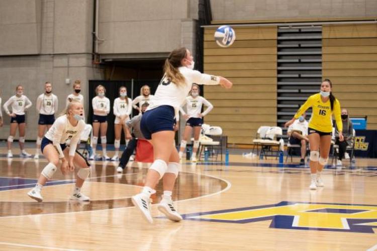 Volleyball action, with one player bumping top set up a spike.