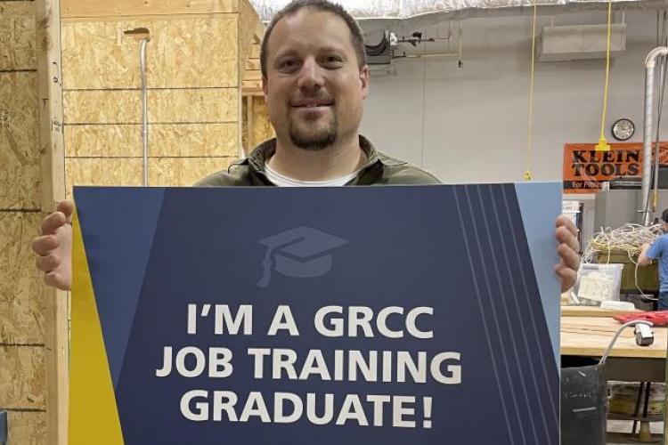 Martin Maloley holding a sign reading "I'm a GRCC Job Training Graduate"