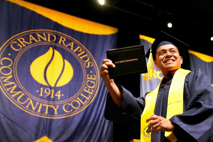 A student holding up his diploma case at commencement.