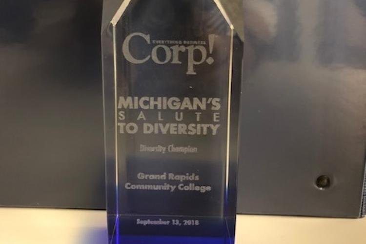 Etched on the glass award, it says: "Corp.! Michigan's Salute to Diversity. Diversity Champion. Grand Rapids Community College. September 13, 2018."