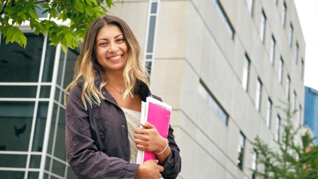GRCC student holding books and smiling while leaving the Science building