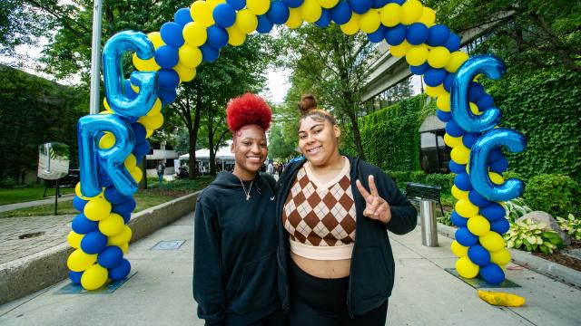 Two students pose near a blue and yellow GRCC balloon arch.