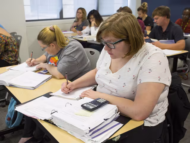 Students work with calculator and book in an accounting class.