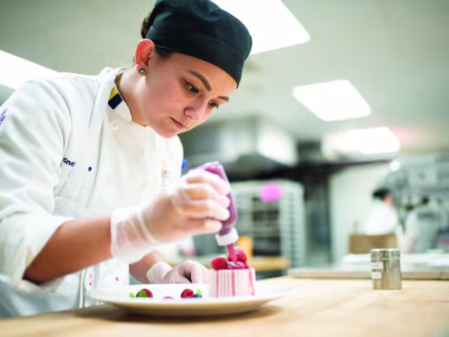 Student dresses a pastry with sauce.