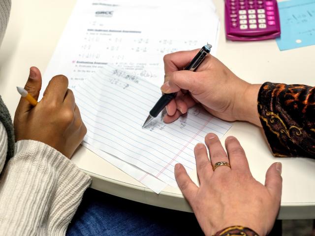 Teacher and student hands working on a math problem.