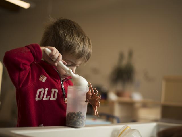 A preschooler stirring a container of rocks with a spatula 