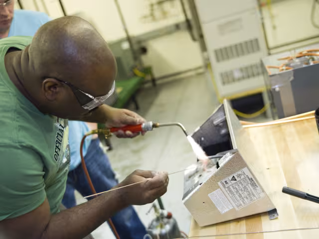 Student soddering a pipe for an HVAC system.