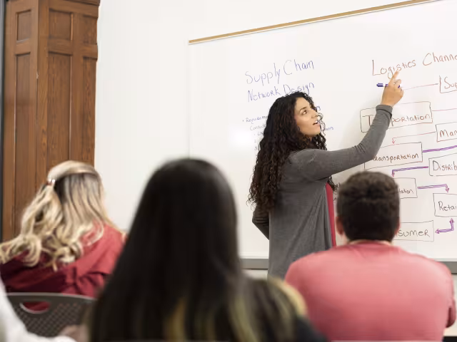 Student pointing to a white board showing logistics channels in a supply chain design.
