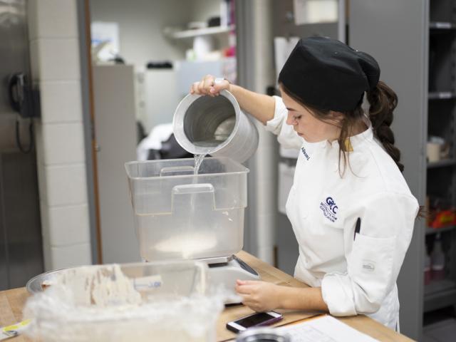 Culinary student pouring flour in to a bowl