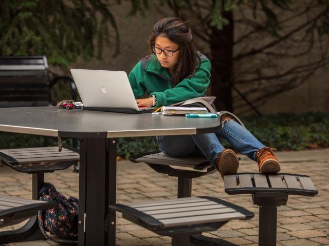 Student working on laptop at a picnic table on the commons