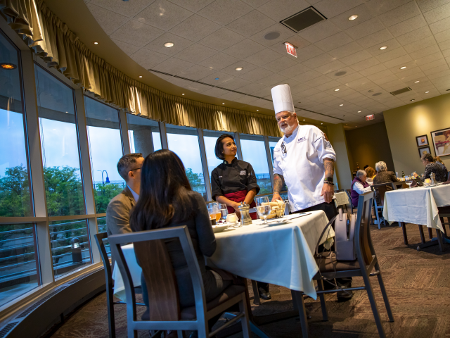 A student in the Pre-Hospitality Management program joins the chef at a table in The Heritage Restaurant.
