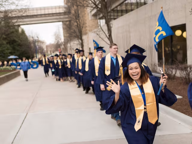 A line of students in cap and gown walking into Commencement.