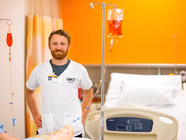 A Nursing program student stands in front of a hospital bed in GRCC's simulation lab.