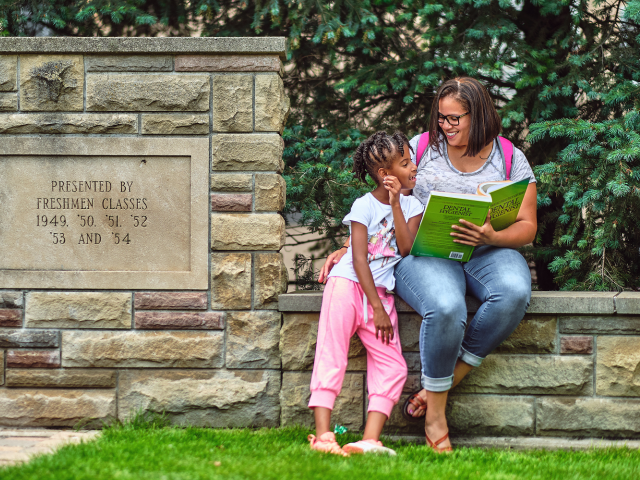 A student looks at her dental hygiene textbook with her daughter on campus.