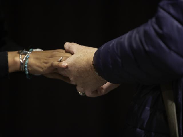 A community member holds hands while paying respect to a speaker at an ODEI event.
