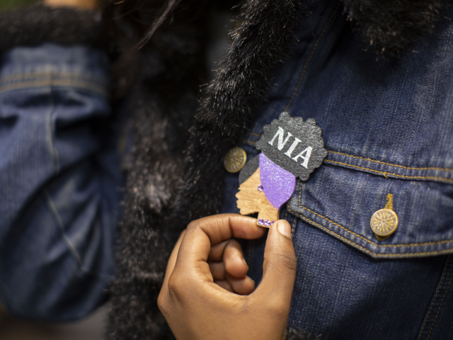 Student touches a NIA pin on their lapel.
