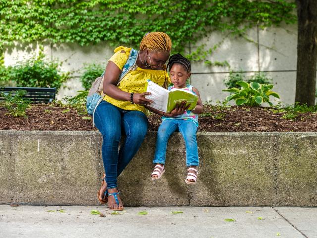 Mother and daughter reading a book together on the bostwick commons. 