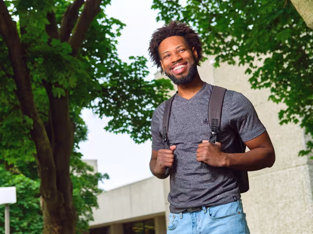 Student holds their backpack, smiling.