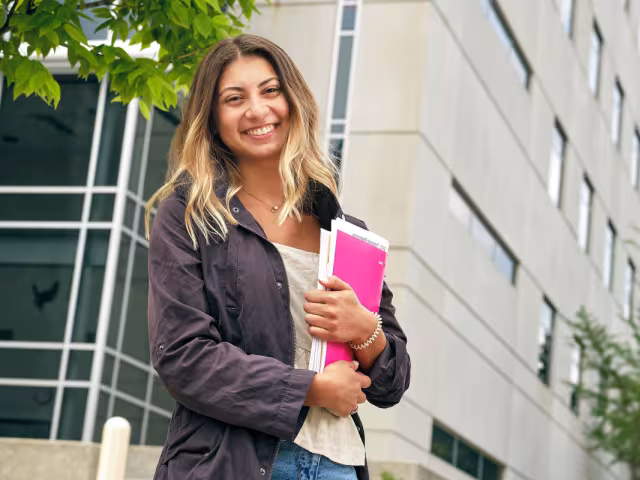GRCC student holding books and smiling while leaving the Science building