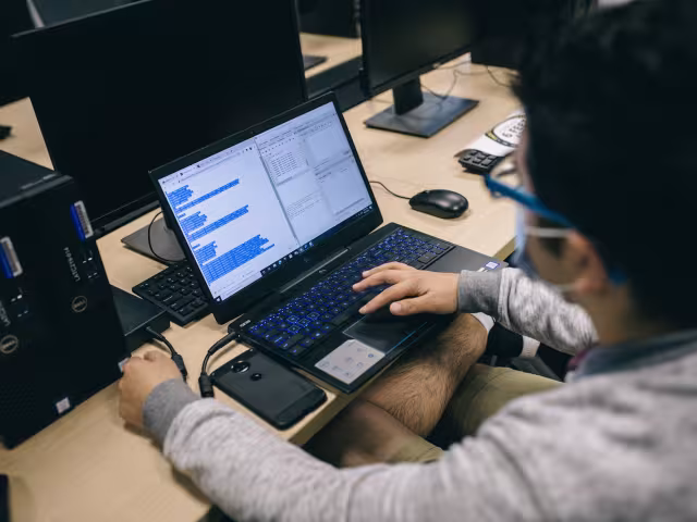 Student writing code on a laptop in class.