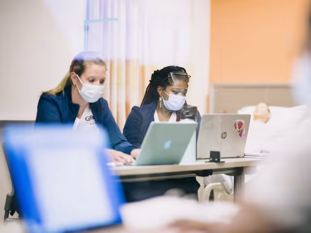 Students in scrubs taking notes in class.