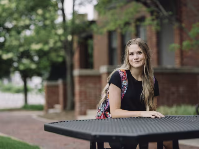 Student sitting at a picnic table outside Sneden Hall