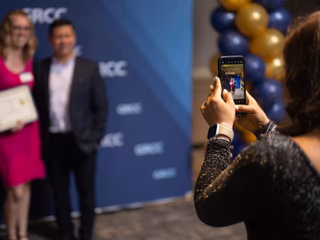 student takes photo of people standing in front of a GRCC backdrop. 