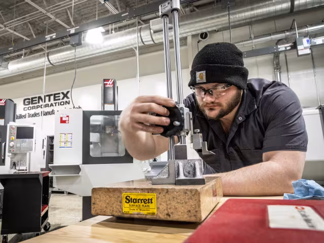 A person adjusts a dial on a device at a workbench.