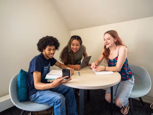 students sitting at a table looking at a cellphone