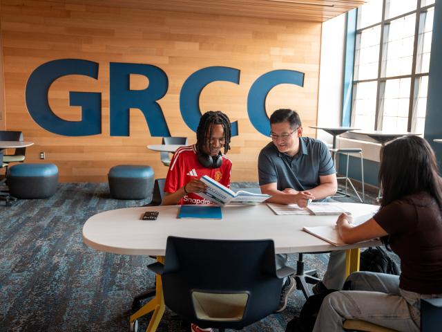 Three people study at a desk together in front of a GRCC wall sign.