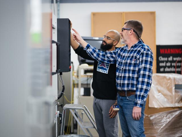 Two people wearing safety glasses work on a large machine.