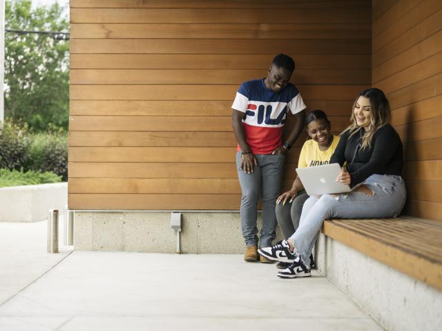Students work on a computer together outdoors.